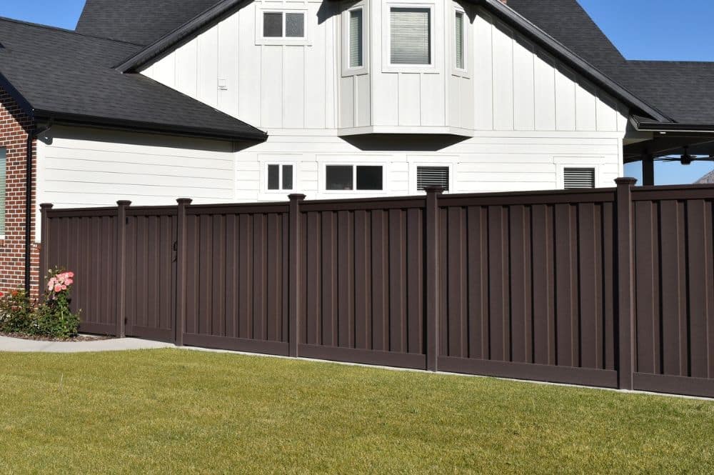 A beautiful tall brown fence by Trex Fencing running along a large white home.