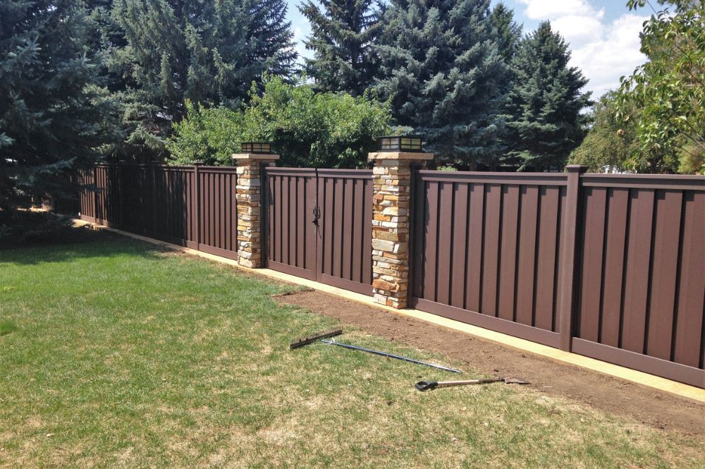 Newly installed brown sense with stone pillars built by Trex Fencing Company